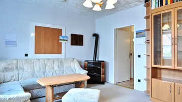 Gemütliches Wohnzimmer mit Kachelofen, Teppichboden und traditioneller Deckenverkleidung.