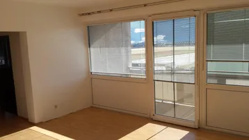 Helles Wohnzimmer mit Parkettboden, großen Fenstern und Zugang zu einem Balkon.