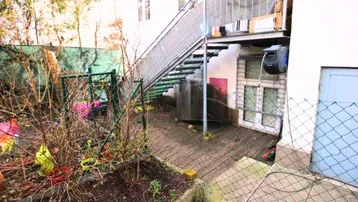 Hinterhofbereich mit Außentreppe, kleiner Gartenfläche und gepflastertem Zugang zu den unteren Räumen.