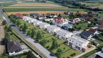 Luftaufnahme einer modernen Reihenhaussiedlung in ländlicher Umgebung mit Photovoltaikanlagen auf den Dächern.