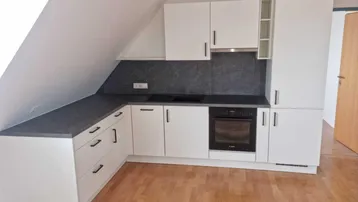 Helle Einbauküche im Dachgeschoss mit weißen Schränken, dunkler Arbeitsplatte und Holzboden.