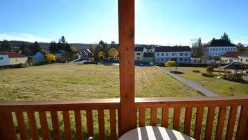 Sonnenverwöhnter Balkon mit Holzboden und weitem Blick über grüne Felder und die umliegende Landschaft.