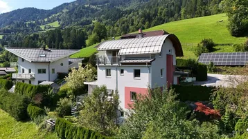 Hausfassade mit mehreren Balkonen und Solaranlage in grüner Berglandschaft.