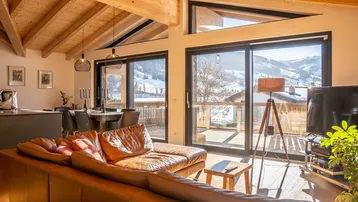 Heller offener Wohn-Essbereich mit Holzbalkendecke, großen Fenstern und Bergblick.