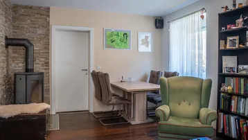 Heller Essbereich mit Holztisch, grünem Sessel und einem modernen Holzofen an der Steinwand.