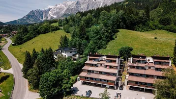 Luftaufnahme einer Wohnanlage in alpiner Landschaft mit Bergen und viel Grün.