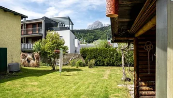 Gepflegter Rasenbereich mit Hecke und Blick auf die umliegende Berglandschaft und moderne Gebäude.