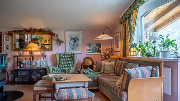 Gemütliches Wohnzimmer mit traditionellen Möbeln, rosa Wänden und Blick auf die grüne Berglandschaft.