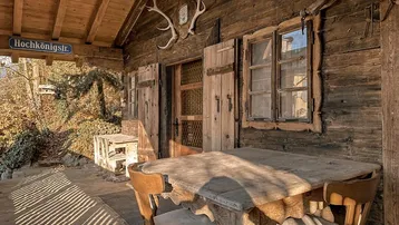 Rustikale Holzterrasse mit traditionellen Möbeln und Hirschgeweih-Dekoration an der Fassade des Chalets.