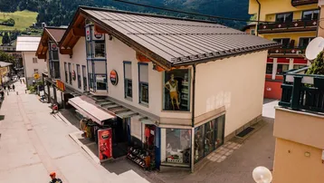 Gebäudeansicht an einer belebten Straße mit Geschäften und Bergkulisse im Hintergrund.