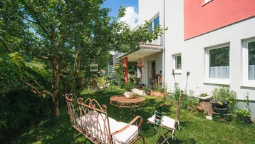Gepflegter Gartenbereich mit Sitzgelegenheiten und Bäumen neben dem Wohnhaus.