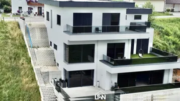 Moderne, mehrstöckige Villa mit Flachdach, großen Fenstern und mehreren Balkonen.