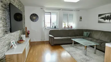 Helles Wohnzimmer mit bequemer Eckcouch, Holzboden und einer modernen Steinwand.