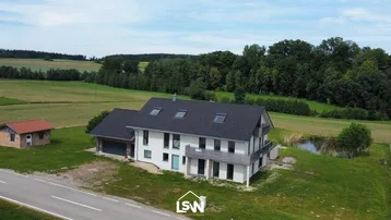 Luftaufnahme eines modernen Wohnhauses in ländlicher Umgebung mit Feldern, Wald und einem kleinen Teich.