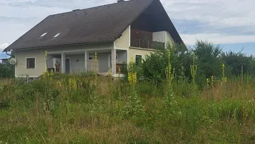 Freistehendes Haus mit Satteldach und Balkon, umgeben von üppigem Grün und ländlicher Natur.