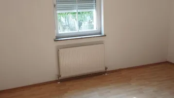 Helles Zimmer mit Laminatboden und Fenster mit Rollladen, ideal für Schlaf- oder Wohnbereich.