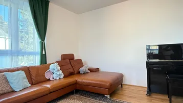 Helles Wohnzimmer mit Ledersofa, Klavier und Blick ins Grüne durch das Fenster.