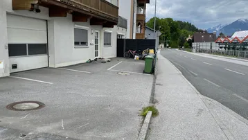 Außenansicht des Gebäudes mit Garagentor und gepflastertem Parkplatz an der Straße.