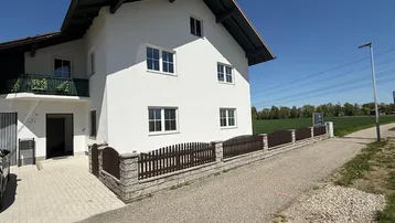 Außenansicht eines modernen Hauses mit weißer Fassade, braunem Dach und kleinem Balkon.