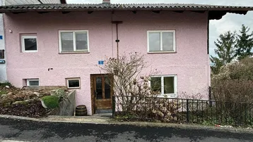 Älteres Wohnhaus mit rosafarbener Fassade und traditioneller Holztür an einer Straße gelegen.