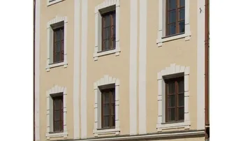 Historische Fassade eines Mehrfamilienhauses mit mehreren Fenstern und einem Geschäftseingang im Erdgeschoss.