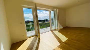 Helles Zimmer mit Parkettboden und direktem Zugang zu einem sonnigen Balkon mit Weitblick.