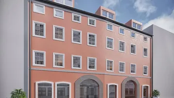 Modernisierte Fassade eines Mehrfamilienhauses mit großen Fenstern und Dachgauben in lebendigem Rotton.