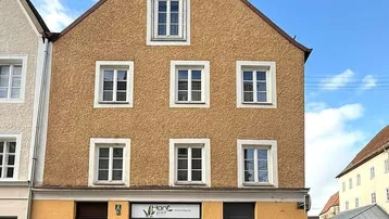 Historisches Gebäude mit ockerfarbener Fassade und Ladenlokal im Erdgeschoss unter blauem Himmel.