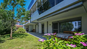 Große Terrasse mit Gartenmöbeln und angrenzender Rasenfläche vor dem modernen Gebäude.