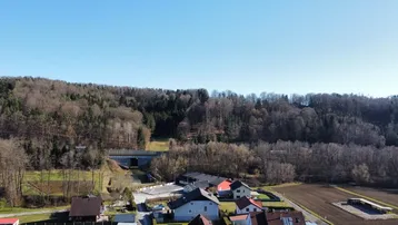 Weitläufige Landschaftsaufnahme mit bewaldeten Hügeln und ländlicher Bebauung in der Ferne.