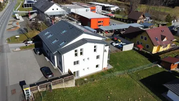 Luftaufnahme eines modernen Wohngebäudes mit Satteldach, Photovoltaikanlage und umliegender Bebauung.