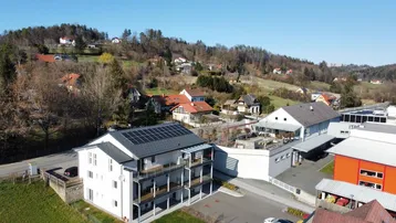 Luftaufnahme eines modernen Mehrfamilienhauses mit Solaranlage auf dem Dach in ländlicher Umgebung.