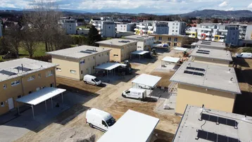 Drohnenaufnahme einer Neubausiedlung mit mehreren Gebäuden und Solaranlagen auf den Dächern.
