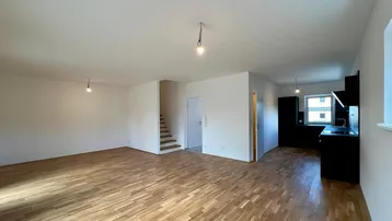 Heller offener Wohnbereich mit Parkettboden und Blick auf die moderne Küche sowie die Treppe.