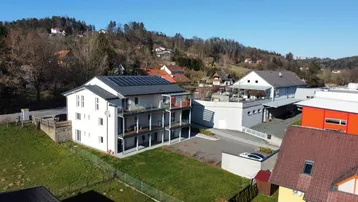 Luftaufnahme des modernen Mehrfamilienhauses mit Solaranlage und umliegender grüner Landschaft.