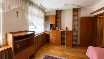 Helles Wohnzimmer mit Fischgrätparkett, Holzmöbeln und einem großen Fenster mit Vorhängen.