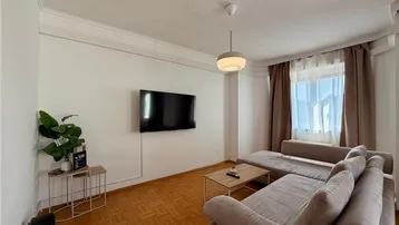 Helles Wohnzimmer mit beigem Ecksofa, Fernseher und Parkettboden.