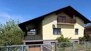 Gelbes Einfamilienhaus mit Satteldach, Balkon und integrierter Garage im Erdgeschoss.