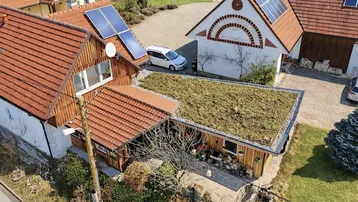 Luftaufnahme eines Hauses mit Ziegeldach, Solaranlage und begrüntem Carport in ländlicher Umgebung.