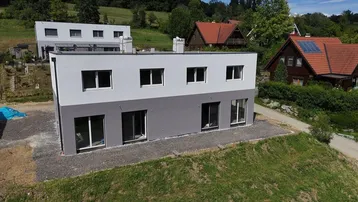 Moderne Doppelhaushälfte im Bau mit grauer und weißer Fassade in ländlicher Umgebung.