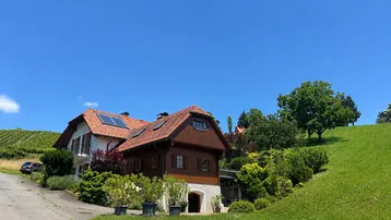 Haus in ländlicher Umgebung mit Photovoltaikanlage auf dem Dach und Weinbergen im Hintergrund.