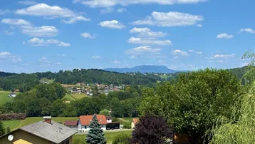 Malerischer Ausblick auf eine ländliche Siedlung mit grünen Hügeln und Bergen im Hintergrund.