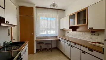 Funktionale Küche mit weißen Schränken, Holztheke und Fenster mit Blick ins Grüne.