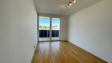 Helles Zimmer mit Holzboden und Zugang zu einem Balkon, ideal als Wohn- oder Schlafbereich.