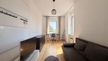 Helles Wohnzimmer mit Holzboden, einem Sofa und einem Arbeitsbereich am Fenster.