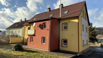 Mehrere Wohnhäuser mit farbigen Fassaden und Satteldächern unter blauem Himmel in ländlicher Umgebung.