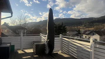 Geräumige Holzterrasse mit weißem Geländer, großem Sonnenschirm und weitem Blick auf die Berge.
