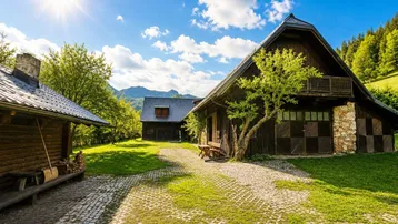 Rustikales Holzhaus mit gepflastertem Hof und grüner Umgebung unter strahlendem Sonnenschein.