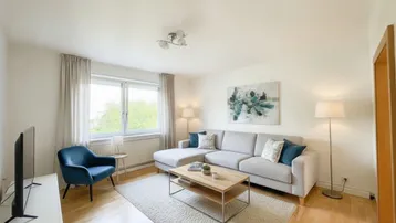 Gemütliches Wohnzimmer mit modernem Sofa, Holzboden und Blick ins Grüne durch das Fenster.