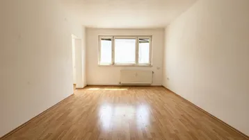 Helles, leeres Zimmer mit Laminatboden und Fenster, bereit zur individuellen Gestaltung.